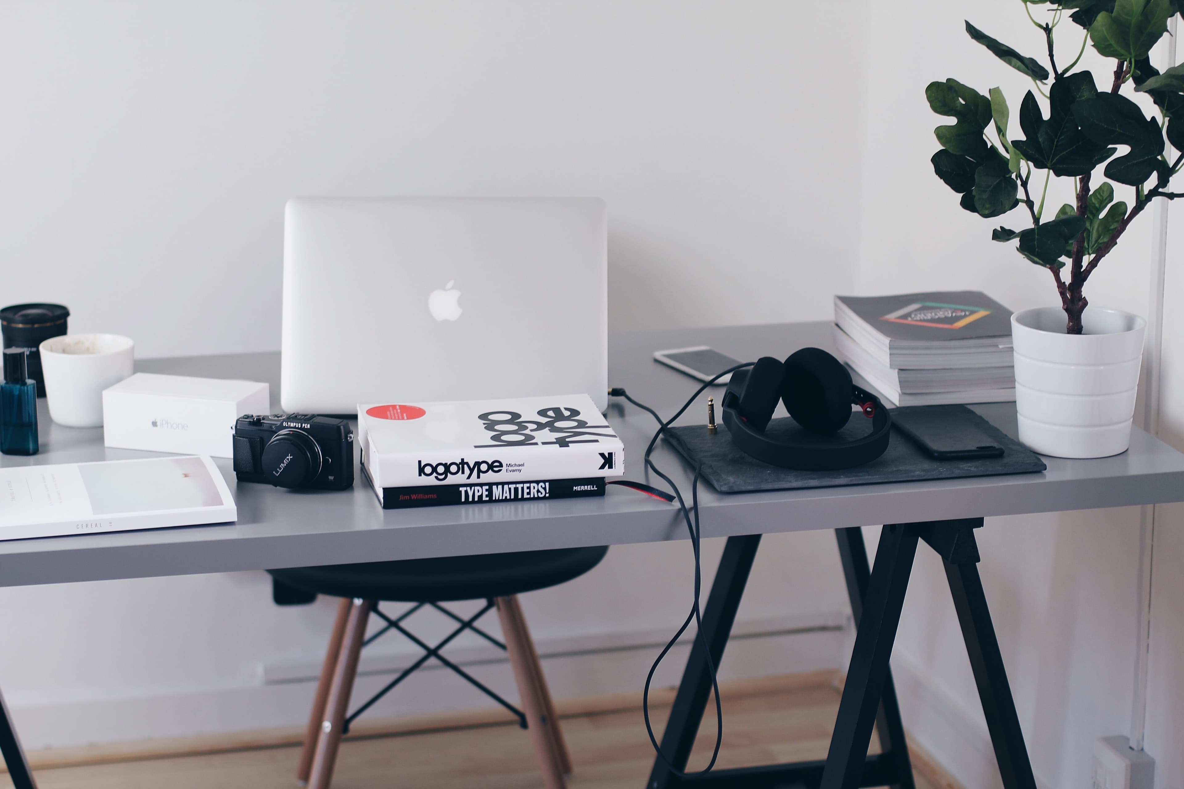 A desk with books, headphones, a phone an a MacBook on it.